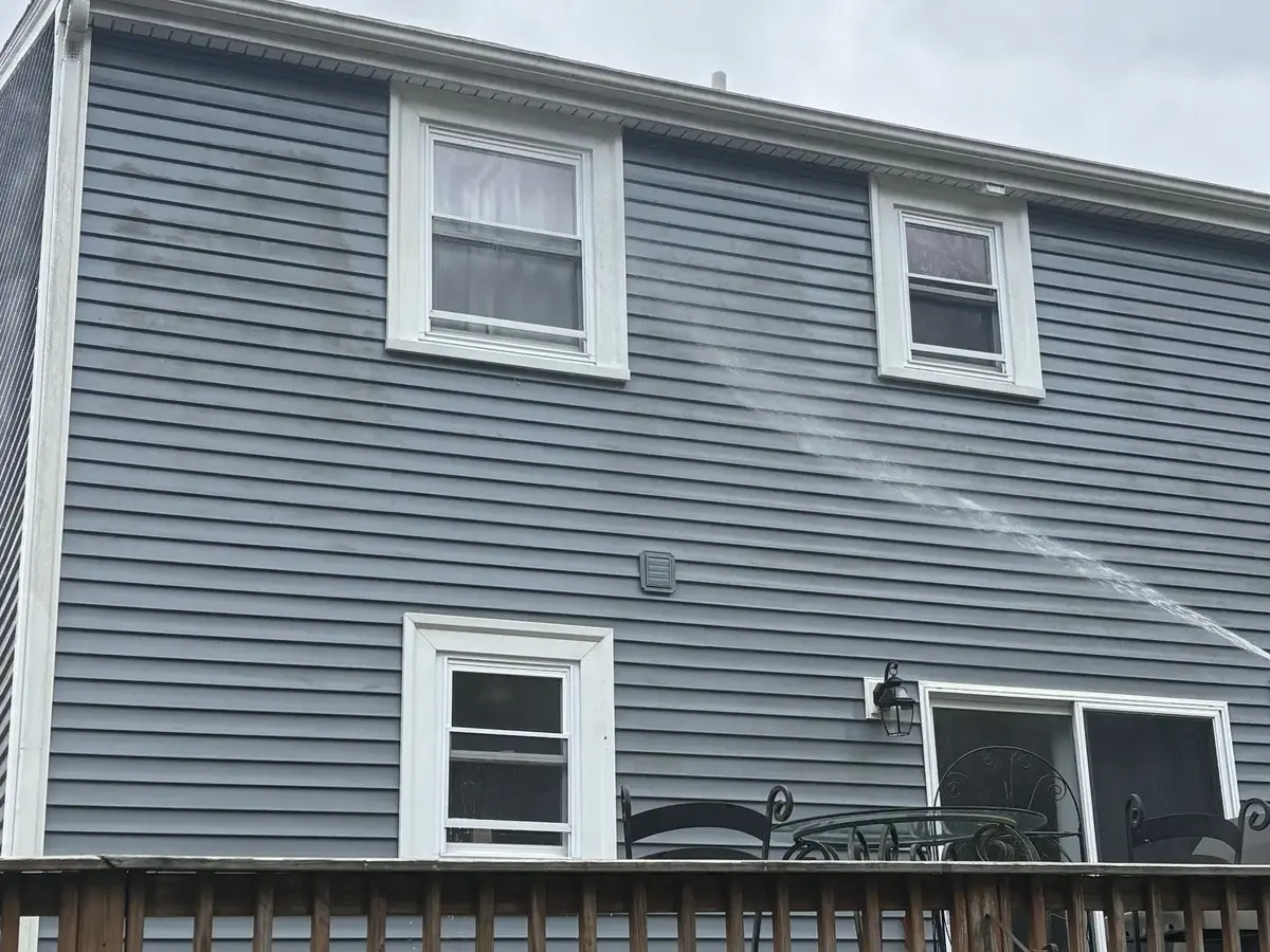 Gray vinyl siding with dirt streaks and algae stains being soft washed in Bellingham MA