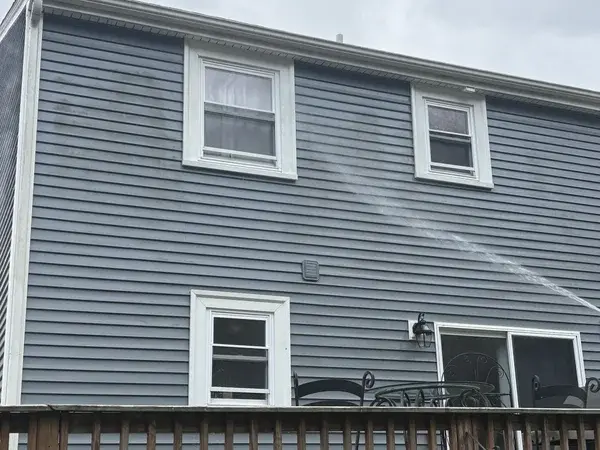 Gray vinyl siding with dirt streaks and algae stains being soft washed in Bellingham MA