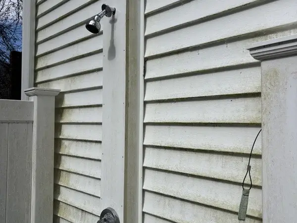 White vinyl siding around outdoor shower with green algae and mildew before soft washing in Franklin MA