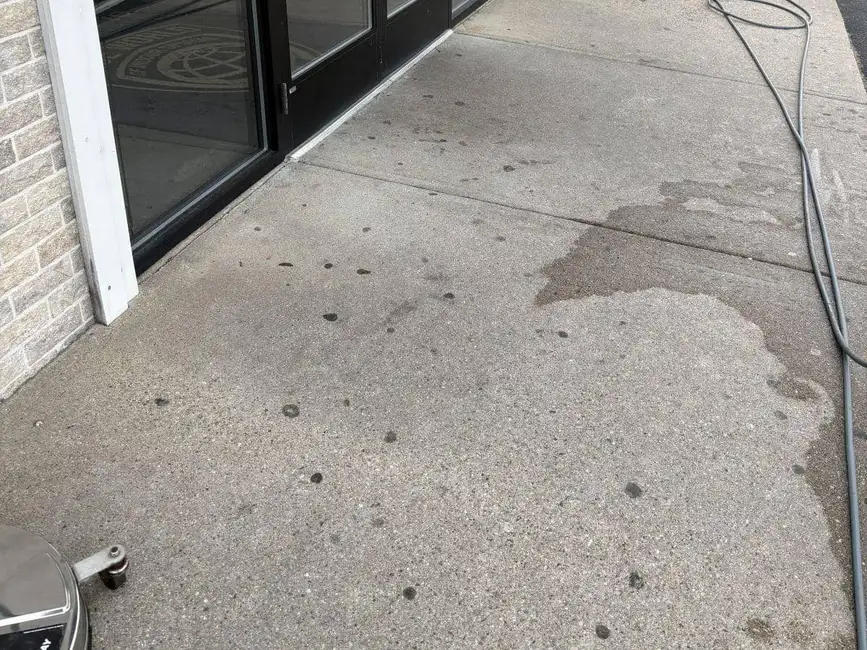 Storefront sidewalk before gum stain removal, covered in black gum spots