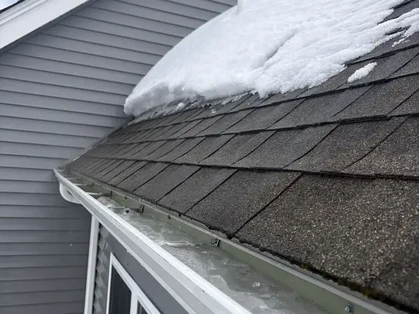 Roof edge with shingles and gutters visible after ice dam removal