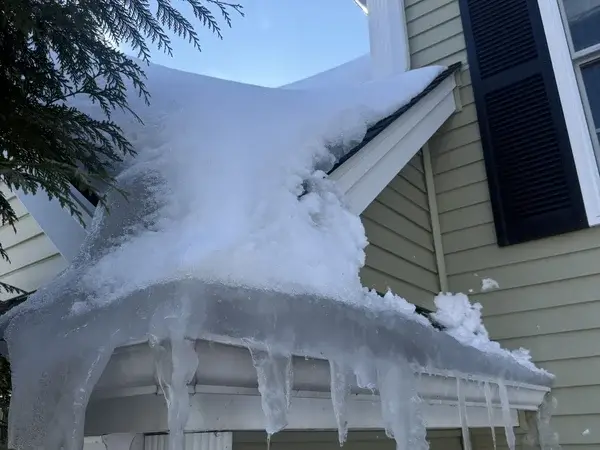 Porch roof with massive ice dam and icicle buildup before removal