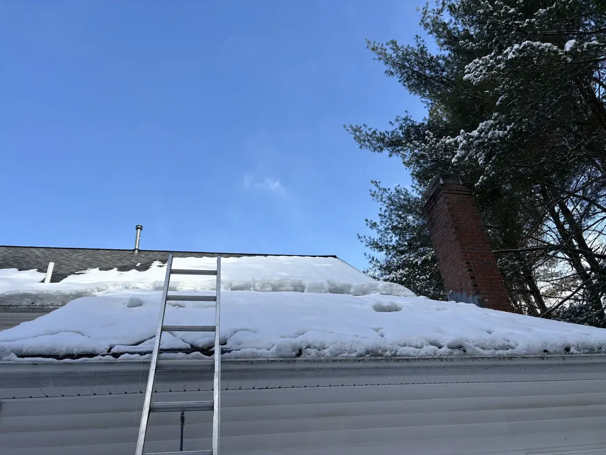 Snow-covered residential roof with ladder before ice dam removal