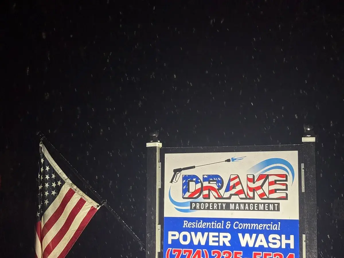 Drake Power Washing service sign with American flag during snowfall at night