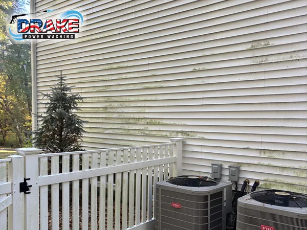 Algae-streaked vinyl siding beside a white railing and AC units before house washing in Franklin MA