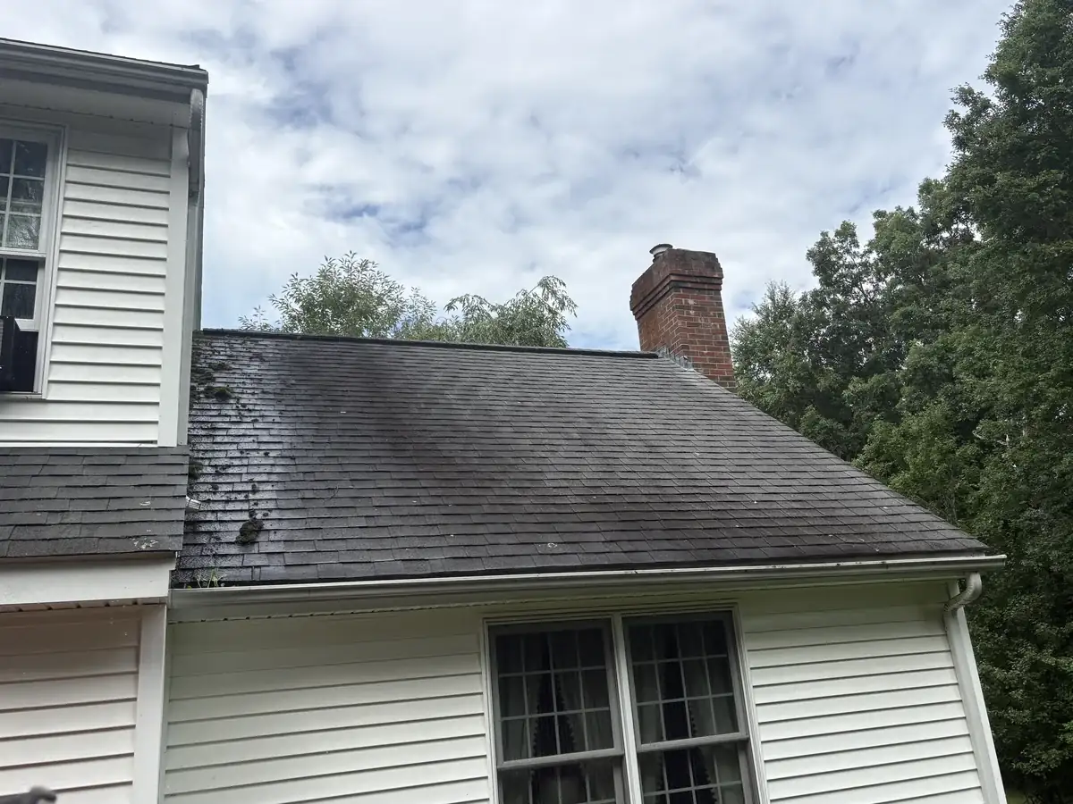 Heavily blackened roof by a brick chimney in Northbridge MA before cleaning